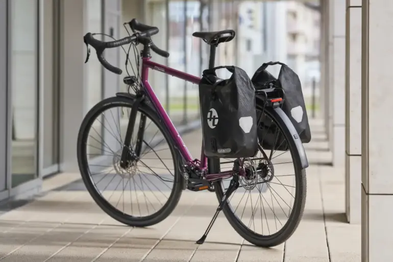Lila Tout Terrain Tribeca Fahrrad mit Rennlenker und Ortlieb-Gepäcktaschen.
