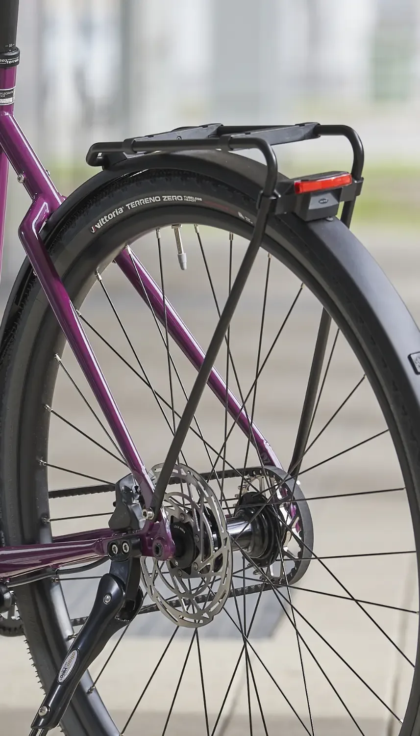 Detailbild des Hinterrads eines violetten Tout Terrain Tribeca Fahrrads mit Scheibenbremse, Gepäckträger und Schutzblech.