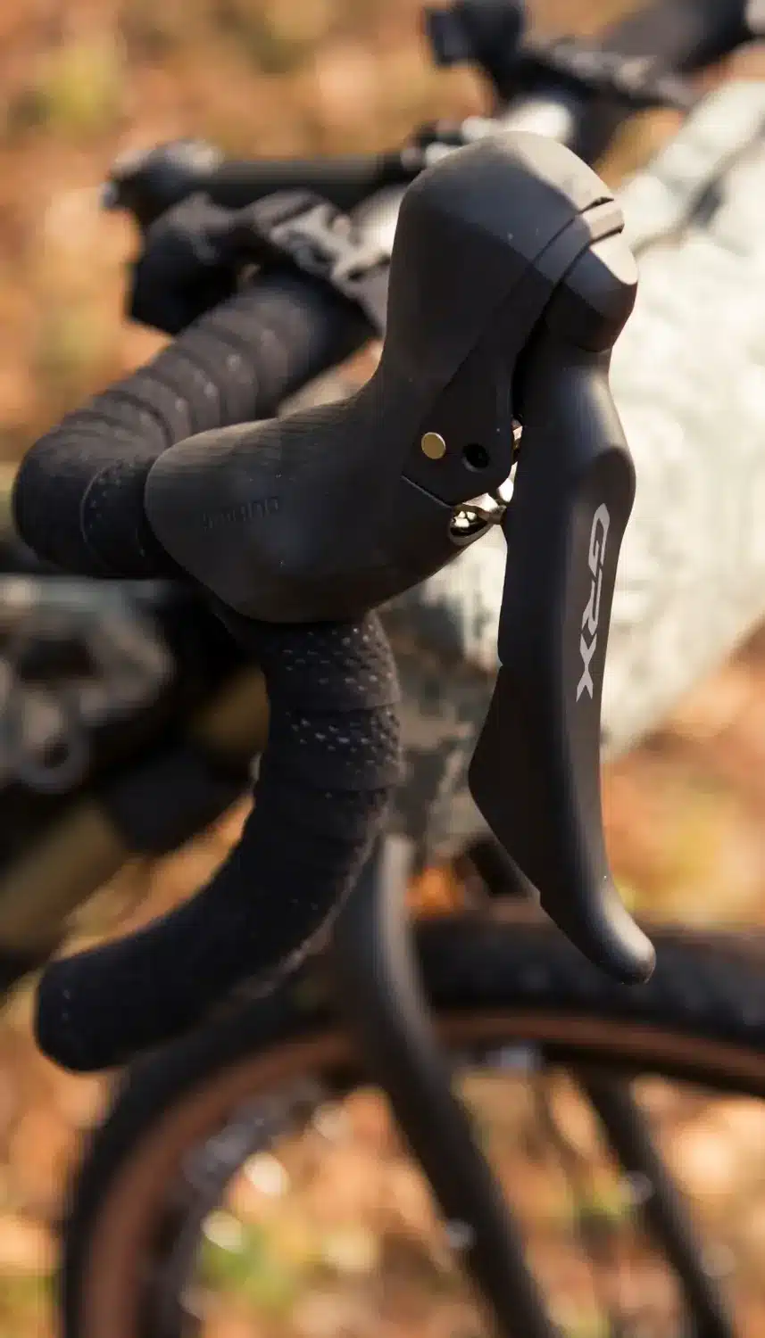 Nahaufnahme eines schwarzen Shimano GRX Schaltbremshebels mit silhouettiertem GRX-Logo, montiert an einem Fahrradlenker mit schwarzem Lenkerband.