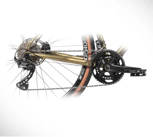 Detailaufnahme des goldfarbenen Stahlrahmens eines Vasco GT 28 Custom Fahrrads, zeigt die Hinterradnabe, Kassette, Schaltwerk, Kette, Kurbelgarnitur und ein Pedal.