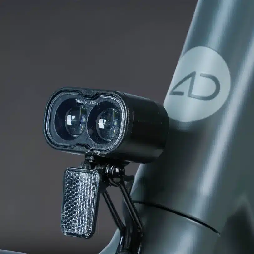 Detail des vorderen Fahrradlichts und des ADO-Logos an einem dunklen Fahrradrahmen