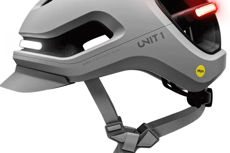 Grauer UNIT 1 AURA Mips Smart-Helm mit integriertem weißem Frontlicht und rotem Rücklicht, Mips-Logo und Belüftungsöffnungen.