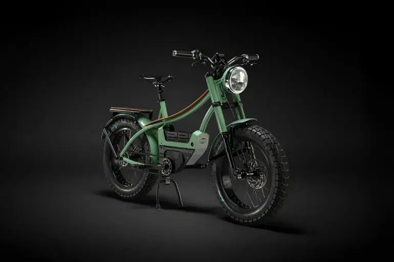 Ein grünes Heritage Heroes Club E-Bike steht auf schwarzem Hintergrund. Das Fahrrad hat einen robusten Chromoly-Stahlrahmen, breite Reifen und eine integrierte Motor- und Batterielösung.