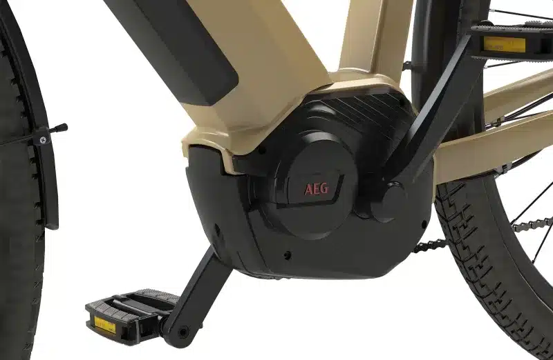 Detailaufnahme des AEG Comfort Drive Mittelmotors an einem sandfarbenen E-Trekkingrad, gezeigt werden die Kurbelgarnitur, das Pedal und Teile des Rahmens und Hinterrads.