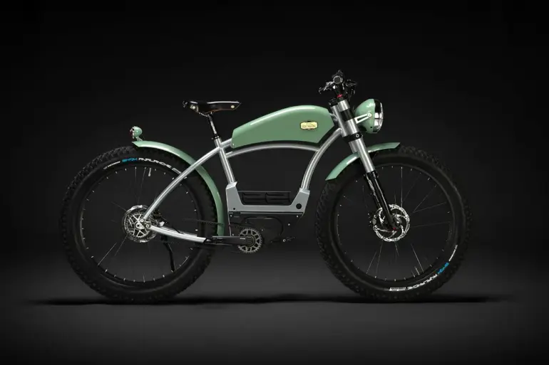 Grünes E-Bike mit Stahlrahmen und breiten Reifen im Stil eines klassischen Motorrads, präsentiert vor schwarzem Hintergrund.