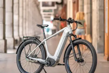 Graues Heritage Style E-Bike mit Federgabel und Gepäckträger, stehend auf einem Gehweg vor einer Säulenarkade.