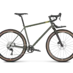 Ein grünes Hobo Dropbar Gravel-Rad steht im Profil. Es hat einen matten Stahlrahmen, Dropbar-Lenker, einen kleinen Frontträger, breite WTB Venture 47 Reifen und eine Shimano GRX Schaltung.