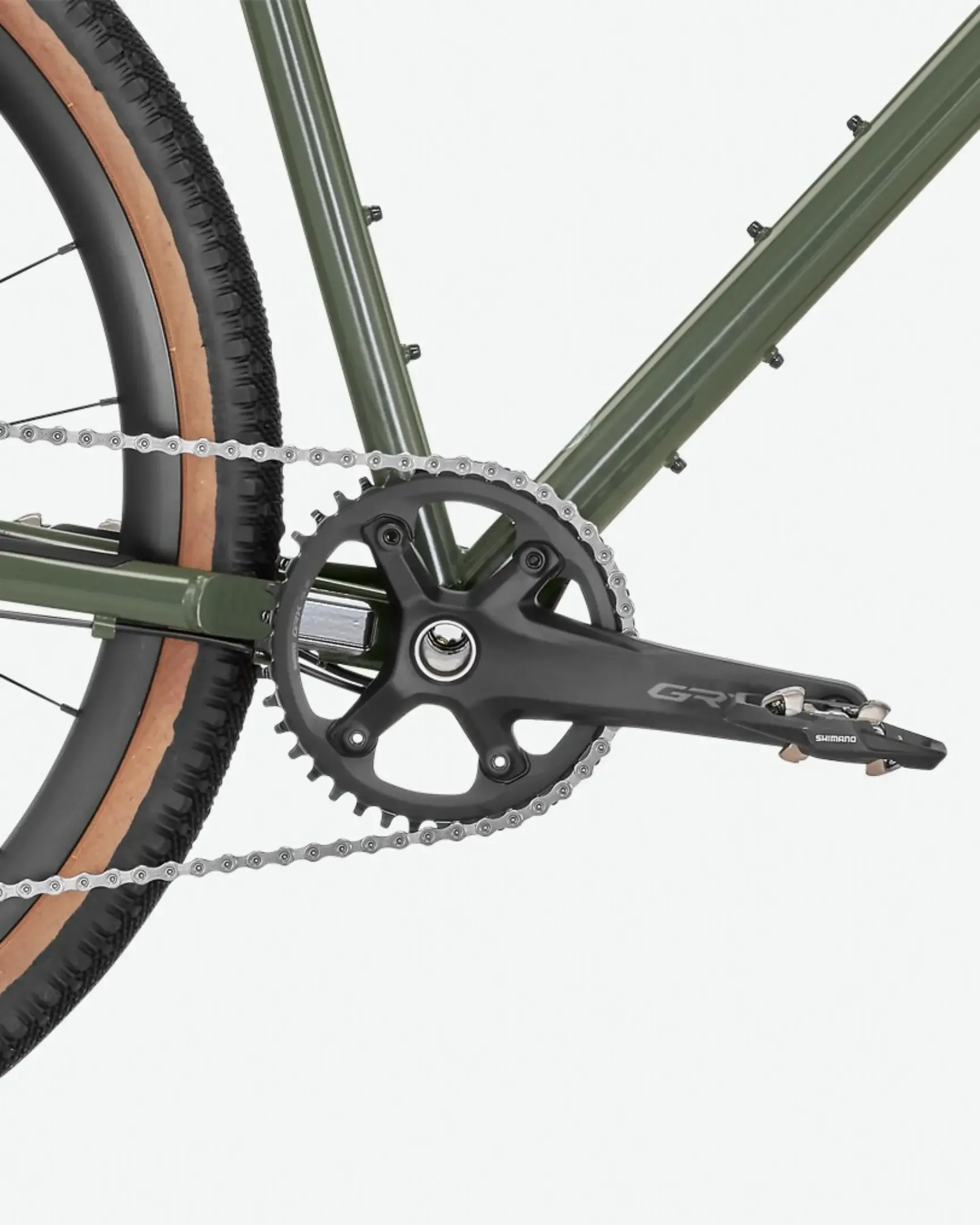 Nahaufnahme der dunklen Kurbelgarnitur mit Shimano GRX-Schriftzug, der silbernen Kette und des breiten, braunen Gravelreifens eines olivgrünen Stahlrahmen-Fahrrads.