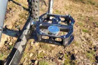 Nahaufnahme eines magped Enduro2 Fahrradpedals in Schwarz mit silbernem Magneten, montiert an einer Fahrradkurbel. Das Pedal zeigt blaue Schrauben und das Logo "magped".