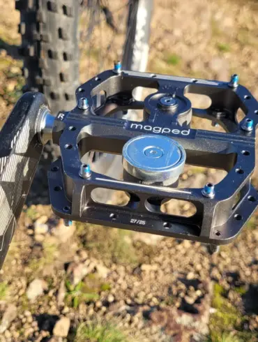 Nahaufnahme eines magped Enduro2 Fahrradpedals in Schwarz mit silbernem Magneten, montiert an einer Fahrradkurbel. Das Pedal zeigt blaue Schrauben und das Logo "magped".