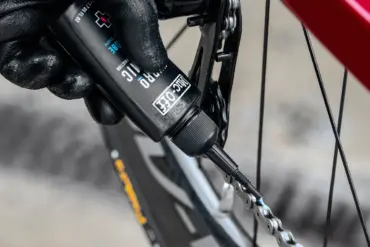 Nahaufnahme einer Hand mit schwarzem Handschuh, die Muc-Off Hydrodynamic Lube auf eine Fahrradkette aufträgt.