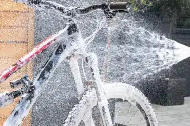 Ein Mountainbike wird mit dem Muc-Off Pressure Washer Bicycle Bundle gereinigt, wobei Schaum aufgetragen und mit Wasser abgespritzt wird. Deutlich erkennbar ist die pinke Flasche des Muc-Off Bike Cleaners, die am Hochdruckreiniger befestigt ist.