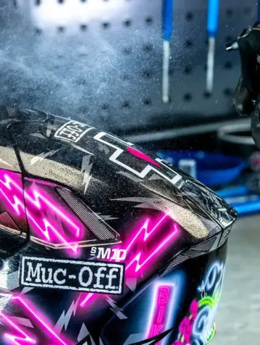 Ein Handschuh sprüht Reiniger auf ein Motorradhelmvisier.