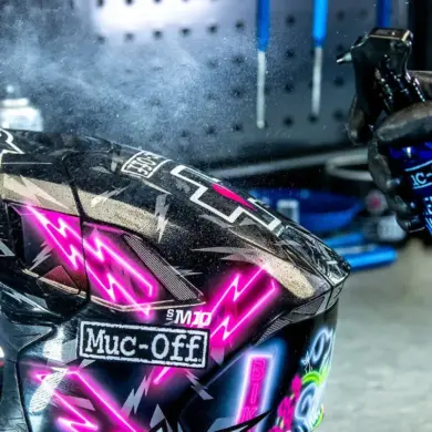 Ein Handschuh sprüht Reiniger auf ein Motorradhelmvisier.