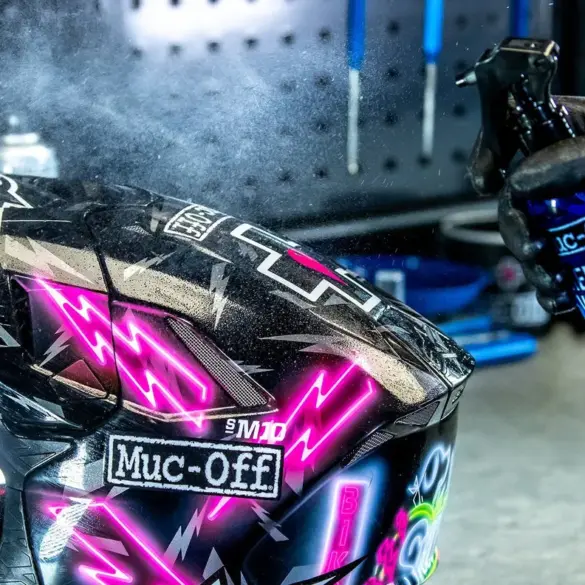 Ein Handschuh sprüht Reiniger auf ein Motorradhelmvisier.