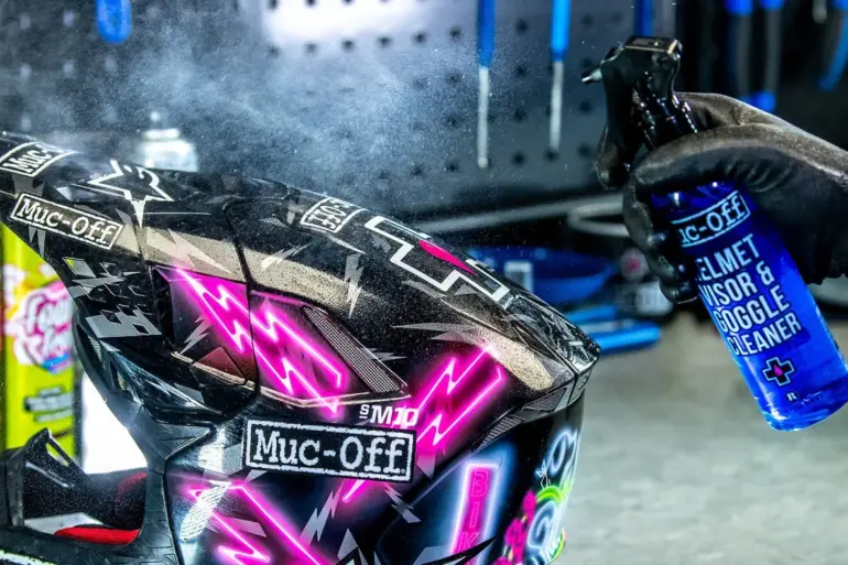 Ein Handschuh sprüht Reiniger auf ein Motorradhelmvisier.