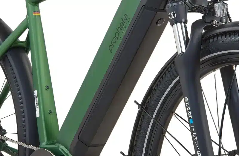 Nahaufnahme des grünen Rahmens eines Prophete Entdecker 4.9 Trekking-E-Bikes. Man sieht den integrierten Akku, die Federgabel und das Vorderrad mit Reifen.