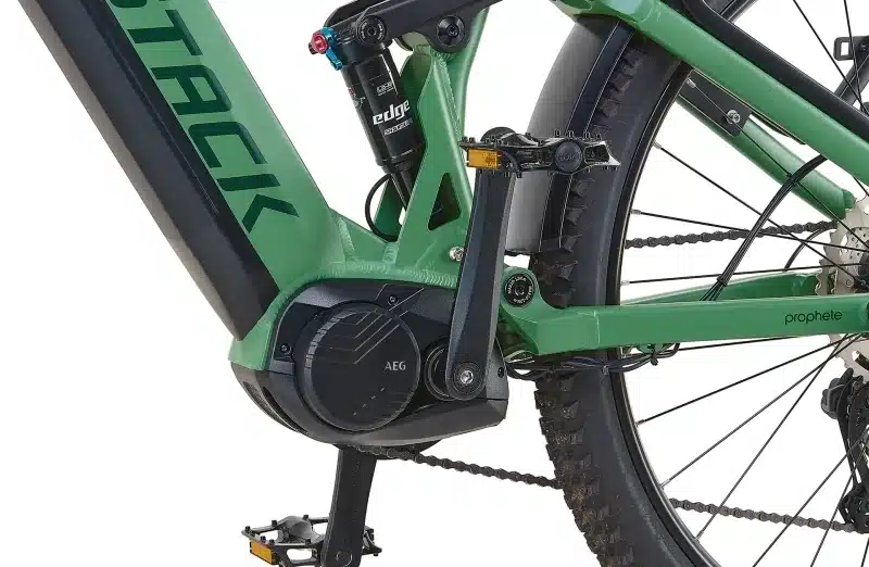 Nahaufnahme des grünen Rahmens mit dem AEG Mittelmotor, der Hinterradaufhängung mit Suntour Dämpfer und der Kette eines Prophete Stack 5.0 29 Elektrofahrrads.