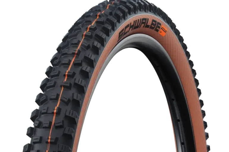 Ein Schwalbe Hans Dampf Super Trail Fahrradreifen mit aggressivem Profil und bronzefarbener Seitenwand, montiert auf einer Felge.