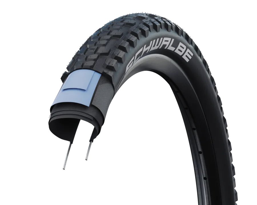 Schnittbild eines Schwalbe Johnny Watts Reifens, der seine breite Lauffläche, das Stollenprofil und die interne Schutzschicht zeigt.