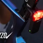 Detailaufnahme eines roten SIGMA Fahrradrücklichts mit der Aufschrift 'SIGMA', montiert an einem blau-violetten Fahrradrahmen.