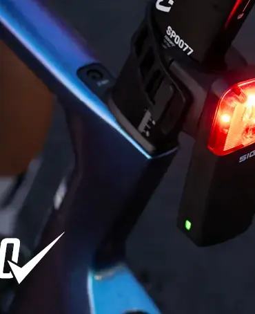 Detailaufnahme eines roten SIGMA Fahrradrücklichts mit der Aufschrift 'SIGMA', montiert an einem blau-violetten Fahrradrahmen.