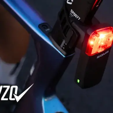 Detailaufnahme eines roten SIGMA Fahrradrücklichts mit der Aufschrift 'SIGMA', montiert an einem blau-violetten Fahrradrahmen.