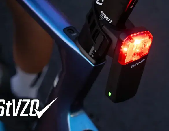 Detailaufnahme eines roten SIGMA Fahrradrücklichts mit der Aufschrift 'SIGMA', montiert an einem blau-violetten Fahrradrahmen.