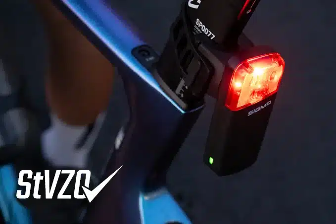 Detailaufnahme eines roten SIGMA Fahrradrücklichts mit der Aufschrift 'SIGMA', montiert an einem blau-violetten Fahrradrahmen.