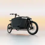 Ein schwarzes TENWAYS CARGO ONE Lastenrad mit breiter Ladebox und integrierter Beleuchtung, steht auf einem neutralen, hellen Untergrund.