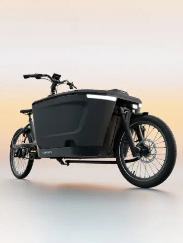 Ein schwarzes TENWAYS CARGO ONE Lastenrad mit breiter Ladebox und integrierter Beleuchtung, steht auf einem neutralen, hellen Untergrund.