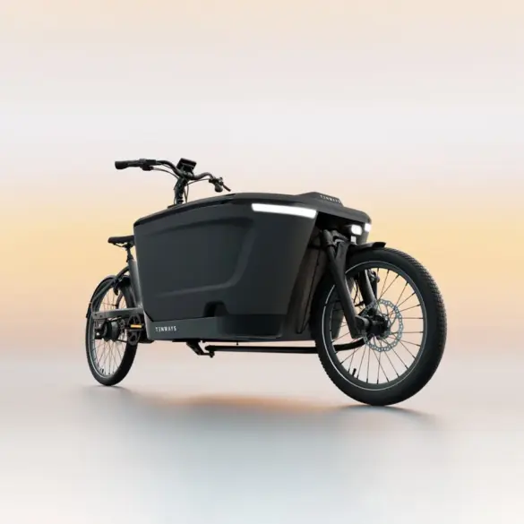 Ein schwarzes TENWAYS CARGO ONE Lastenrad mit breiter Ladebox und integrierter Beleuchtung, steht auf einem neutralen, hellen Untergrund.