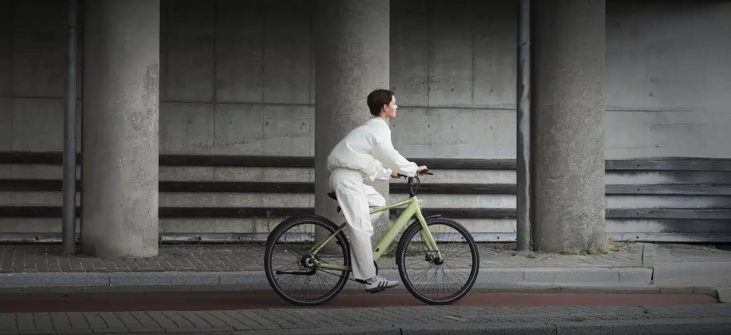 Eine Person in einem weißen Outfit fährt ein hellgrünes TENWAYS CGO600 Pro E-Bike auf einem Radweg. Der Hintergrund zeigt Betonstrukturen und Grautöne.