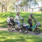 Familie, bestehend aus zwei Erwachsenen und zwei Kindern, fährt auf zwei kompakten Lasten-E-Bikes im Park.