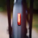 Rotes, rechteckiges Trelock Fahrradrücklicht mit COB-LEDs und Multi-Lens-Technologie, montiert an der Unterseite eines Schutzblechs, leuchtet in der Dunkelheit.