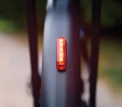 Rotes, rechteckiges Trelock Fahrradrücklicht mit COB-LEDs und Multi-Lens-Technologie, montiert an der Unterseite eines Schutzblechs, leuchtet in der Dunkelheit.