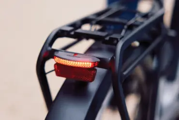Nahaufnahme des roten Trelock LS 653 COB Line Dynamo Rücklichts, montiert an der Gepäckträgervorrichtung eines Fahrrads. Das Licht leuchtet hell.