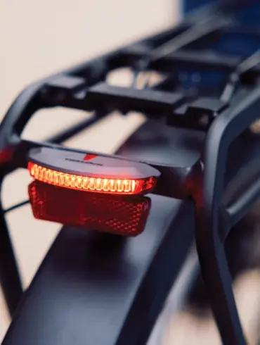 Nahaufnahme des roten Trelock LS 653 COB Line Dynamo Rücklichts, montiert an der Gepäckträgervorrichtung eines Fahrrads. Das Licht leuchtet hell.