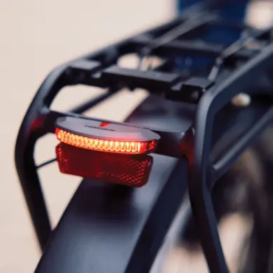 Nahaufnahme des roten Trelock LS 653 COB Line Dynamo Rücklichts, montiert an der Gepäckträgervorrichtung eines Fahrrads. Das Licht leuchtet hell.