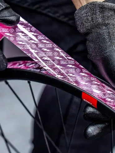 Detailaufnahme von Händen mit schwarzen Muc-Off Handschuhen, die ein pinkes Muc-Off Tubeless Felgenband auf einer schwarzen Fahrradfelge anbringen.