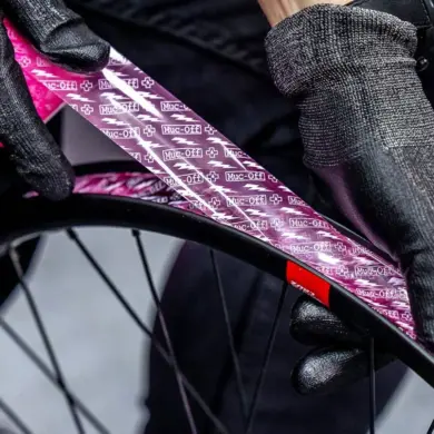 Detailaufnahme von Händen mit schwarzen Muc-Off Handschuhen, die ein pinkes Muc-Off Tubeless Felgenband auf einer schwarzen Fahrradfelge anbringen.