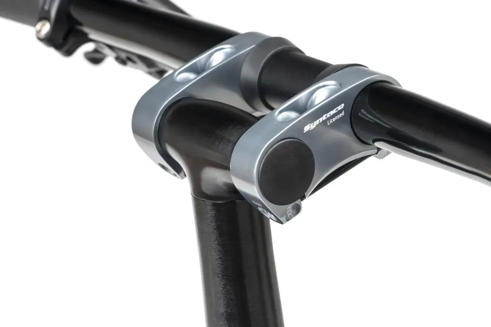 Nahaufnahme der Klemmung eines Syntace VRO Vorbaus an der Lenkerstange eines Fahrrads. Der Vorbau ist aus grauem Metall gefertigt und trägt die Aufschrift 'Syntace Licensed'.