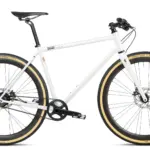 Ein weißes Gravel Bike mit Riemenantrieb und beigen Reifen, stehend vor weißem Hintergrund.
