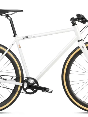 Ein weißes Gravel Bike mit Riemenantrieb und beigen Reifen, stehend vor weißem Hintergrund.
