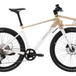 Seitenansicht eines weißen Bulls Clunker Evo E-Bikes mit goldenen Akzenten und einem vorderen Gepäckträger, fotografiert im Studio.