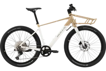 Seitenansicht eines weißen Bulls Clunker Evo E-Bikes mit goldenen Akzenten und einem vorderen Gepäckträger, fotografiert im Studio.