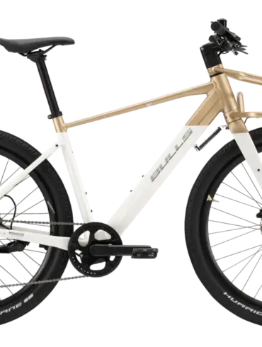 Seitenansicht eines weißen Bulls Clunker Evo E-Bikes mit goldenen Akzenten und einem vorderen Gepäckträger, fotografiert im Studio.
