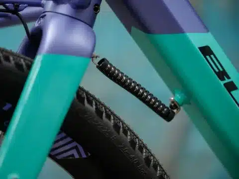 Nahaufnahme des mitlenkenden Frontgepäcksystems am lila-türkisfarbenen Bulls Clunker Evo Fahrrad, mit sichtbarem Federelement und Reifen.
