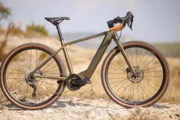 Seitenansicht eines BULLS Grinder EVO SX 2025 Diamant E-Gravelbikes in Olivgrün mit braunen Reifen auf einem Schotterweg im Freien.