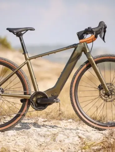 Seitenansicht eines BULLS Grinder EVO SX 2025 Diamant E-Gravelbikes in Olivgrün mit braunen Reifen auf einem Schotterweg im Freien.